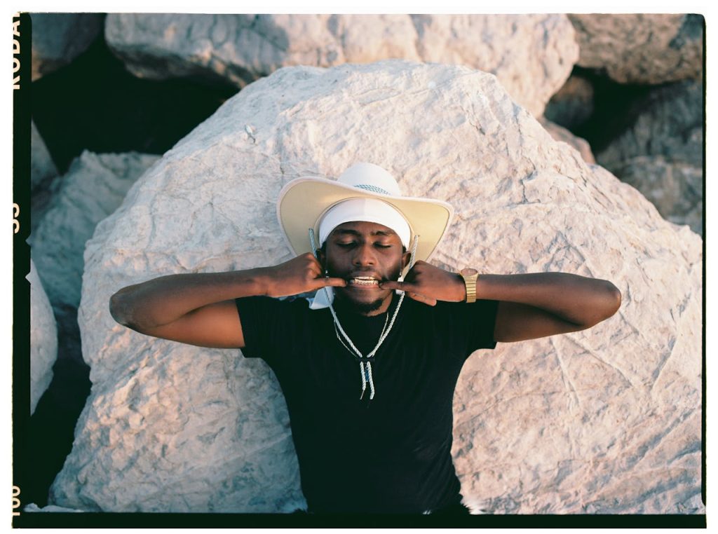 A man in a cowboy hat poses confidently on rocks during sunset.